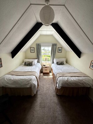 Une chambre avec deux lits, une fenêtre avec des rideaux, une lampe et un luminaire suspendu.