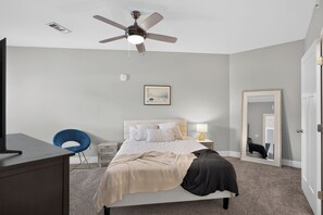 A bedroom with a bed, a desk, a chair, a ceiling fan, a bedside lamp, a framed picture, and a mirror. - Nashville, Brentwood, Nolensville Lux Condo (Nashville)