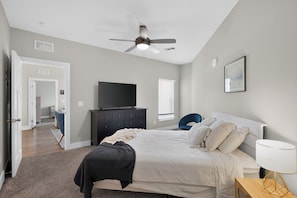 A bedroom with a bed, a TV, a ceiling fan, a window, and a door.