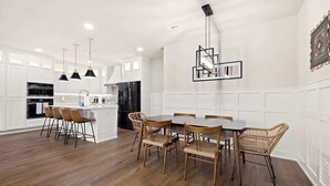Una cocina moderna con armarios blancos, una isla central y un comedor con sillas de madera.