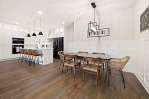 A modern kitchen with white cabinetry, a central island, and a dining area with wooden chairs.