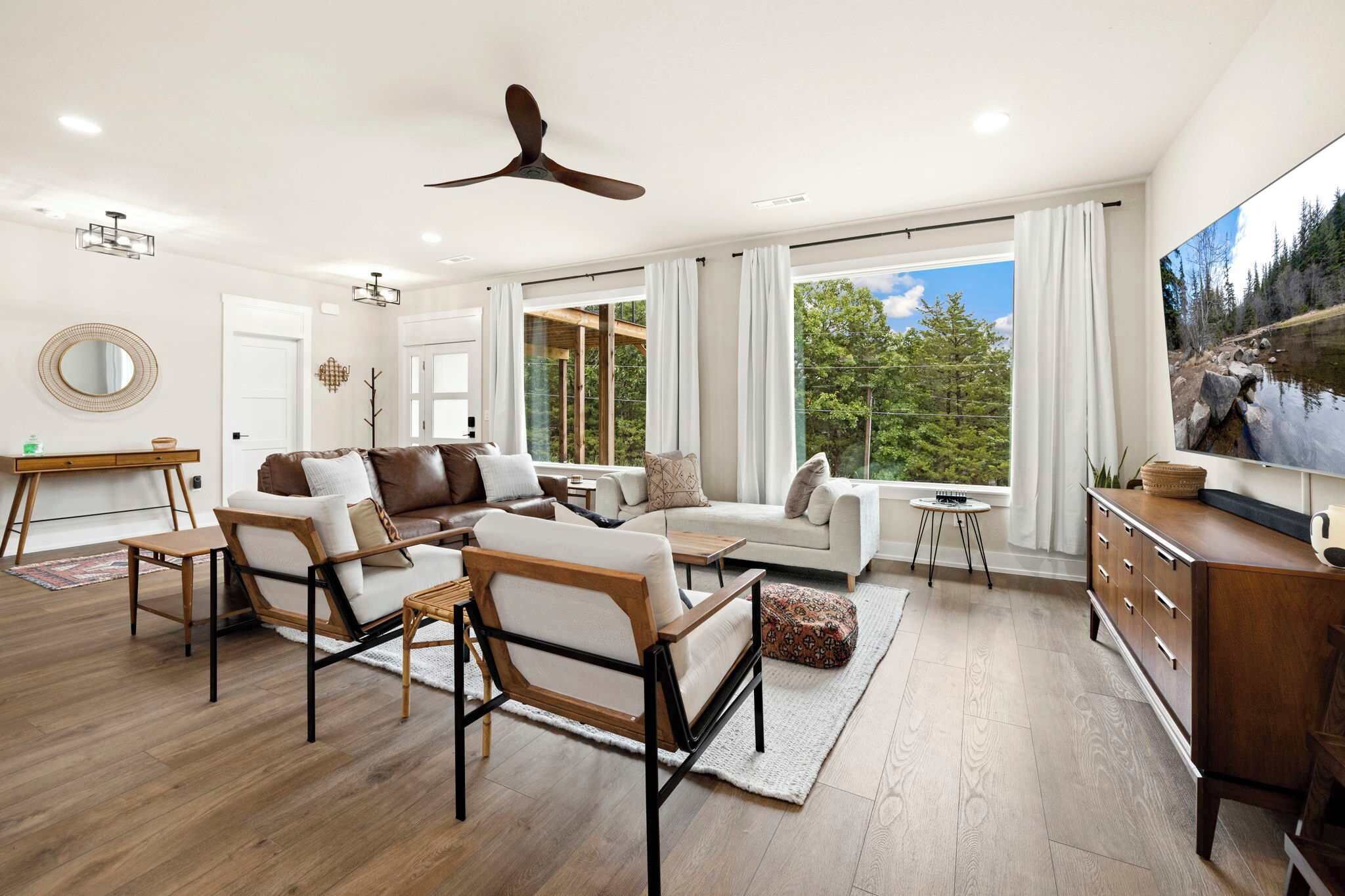 A spacious living room with a large window, a ceiling fan, and a television.
