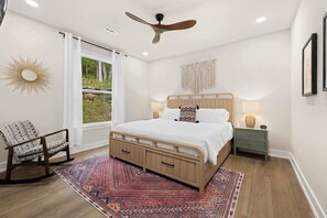 A bedroom with a bed, a chair, a nightstand, a wall-mounted macrame, and a ceiling fan.