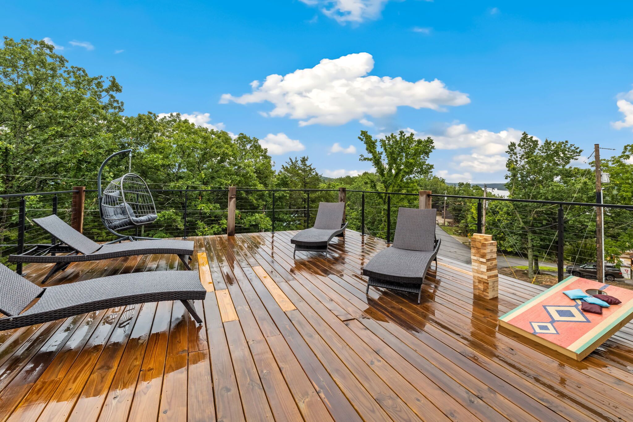 A wooden deck with outdoor furniture, including lounge chairs and a hanging chair, surrounded by trees.