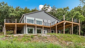 Una casa moderna con una amplia terraza, un espacio al aire libre cubierto y vistas del bosque circundante.