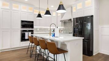 A modern kitchen with white cabinetry, a central island with bar stools, stainless steel appliances, and pendant lighting.