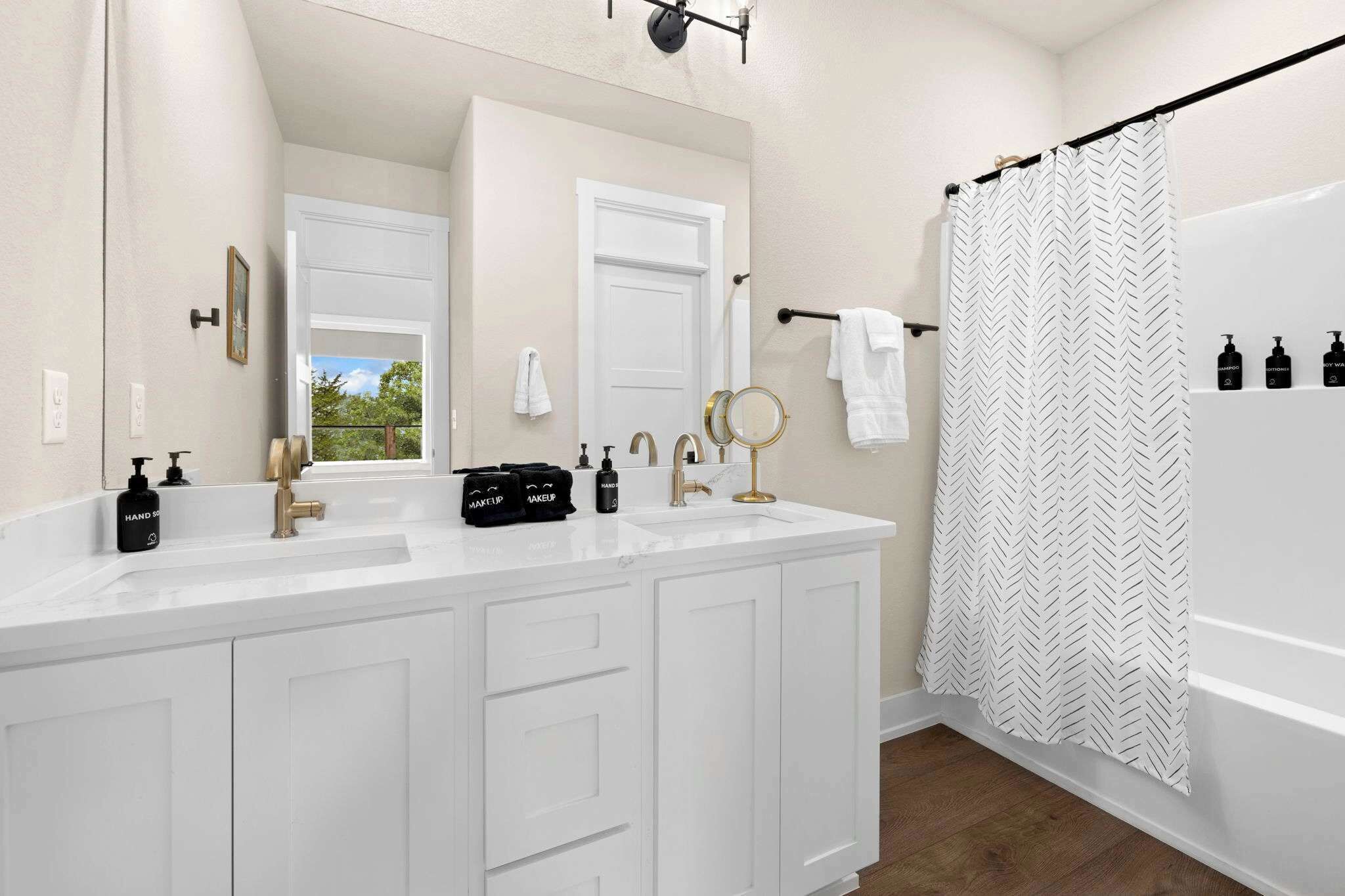 A bathroom with a double vanity, a shower curtain, and a window with a view.
