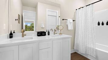A bathroom with a double vanity, a shower curtain, and a window with a view.