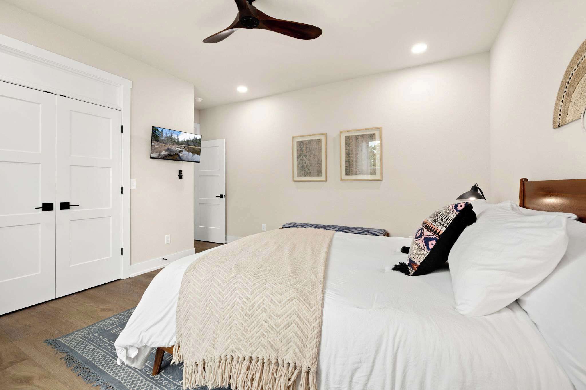 A bedroom with a bed, a ceiling fan, a TV, and framed artwork on the wall.