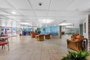 Eine großzügige Lobby mit Fliesenboden, Korbmöbeln und einem Wandbild, das eine Strandansicht zeigt.