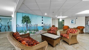 A lounge area with wicker furniture, a mural of a lighthouse, and a view of the sea. - S Hampton 706A Studio Oceanview in Kingston, Pool (Myrtle Beach)
