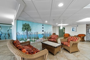 Eine Lounge mit Korbmöbeln, einem Wandbild eines Leuchtturms und Blick auf das Meer.