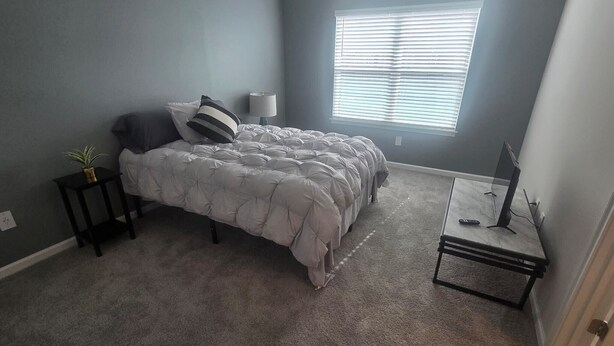 Une chambre à coucher avec un lit, une table de chevet, une lampe et une fenêtre avec des stores.