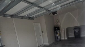 Un garage avec un sol en béton, une porte blanche et un chauffe-eau.