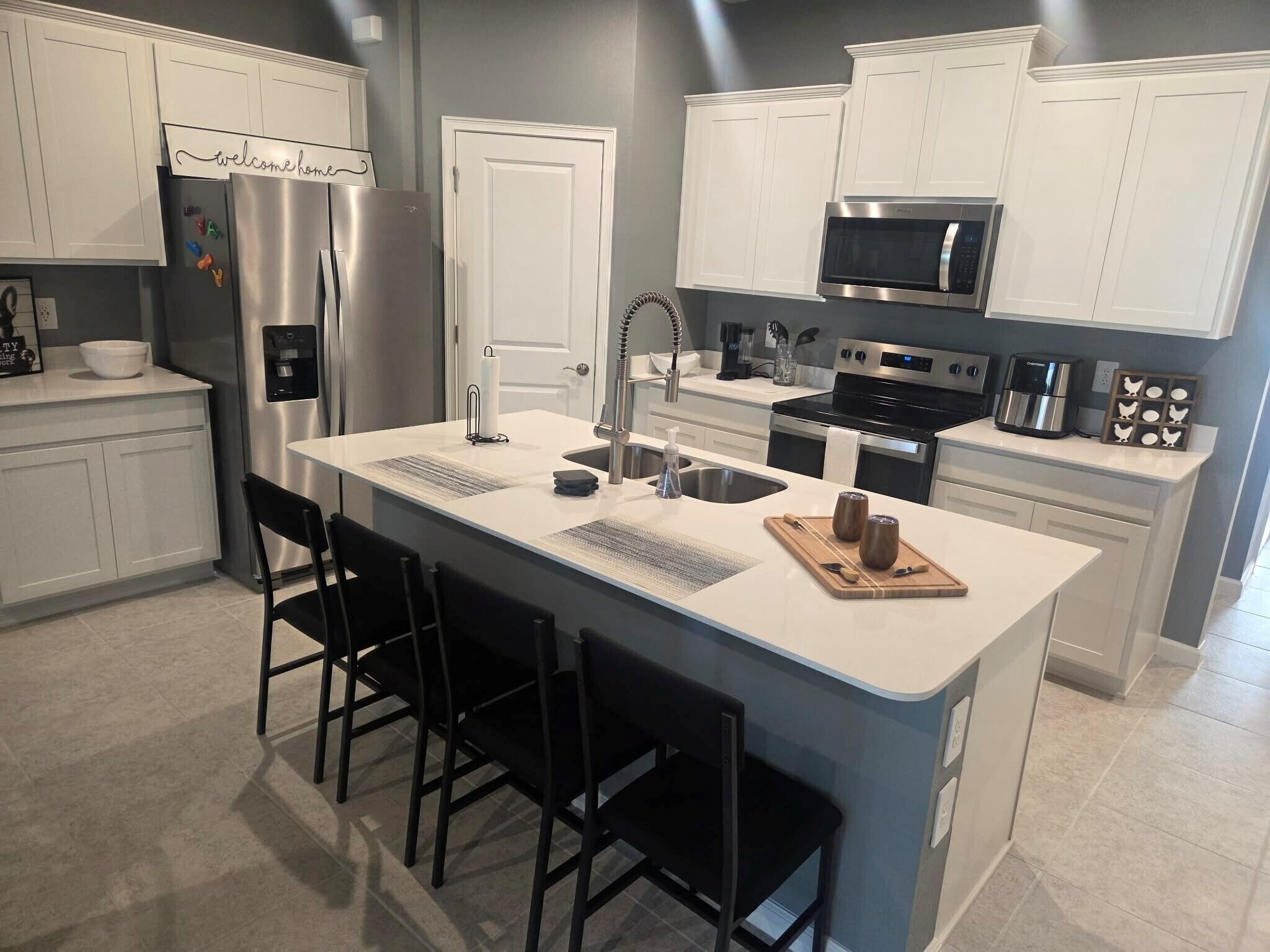 A modern kitchen with white cabinetry, stainless steel appliances, a central island with bar stools, and a microwave above the stove.