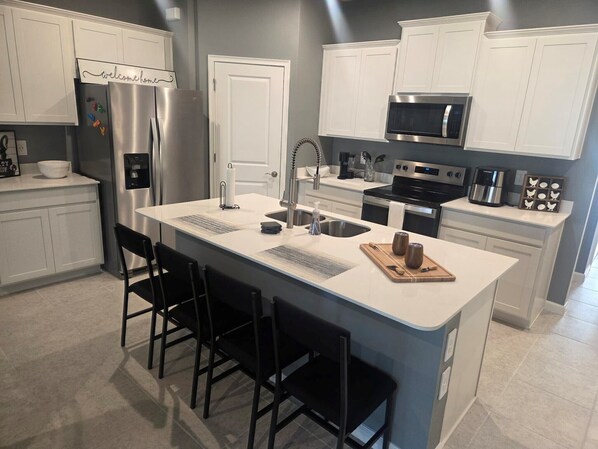 A modern kitchen with white cabinetry, stainless steel appliances, a central island with bar stools, and a microwave above the stove.
