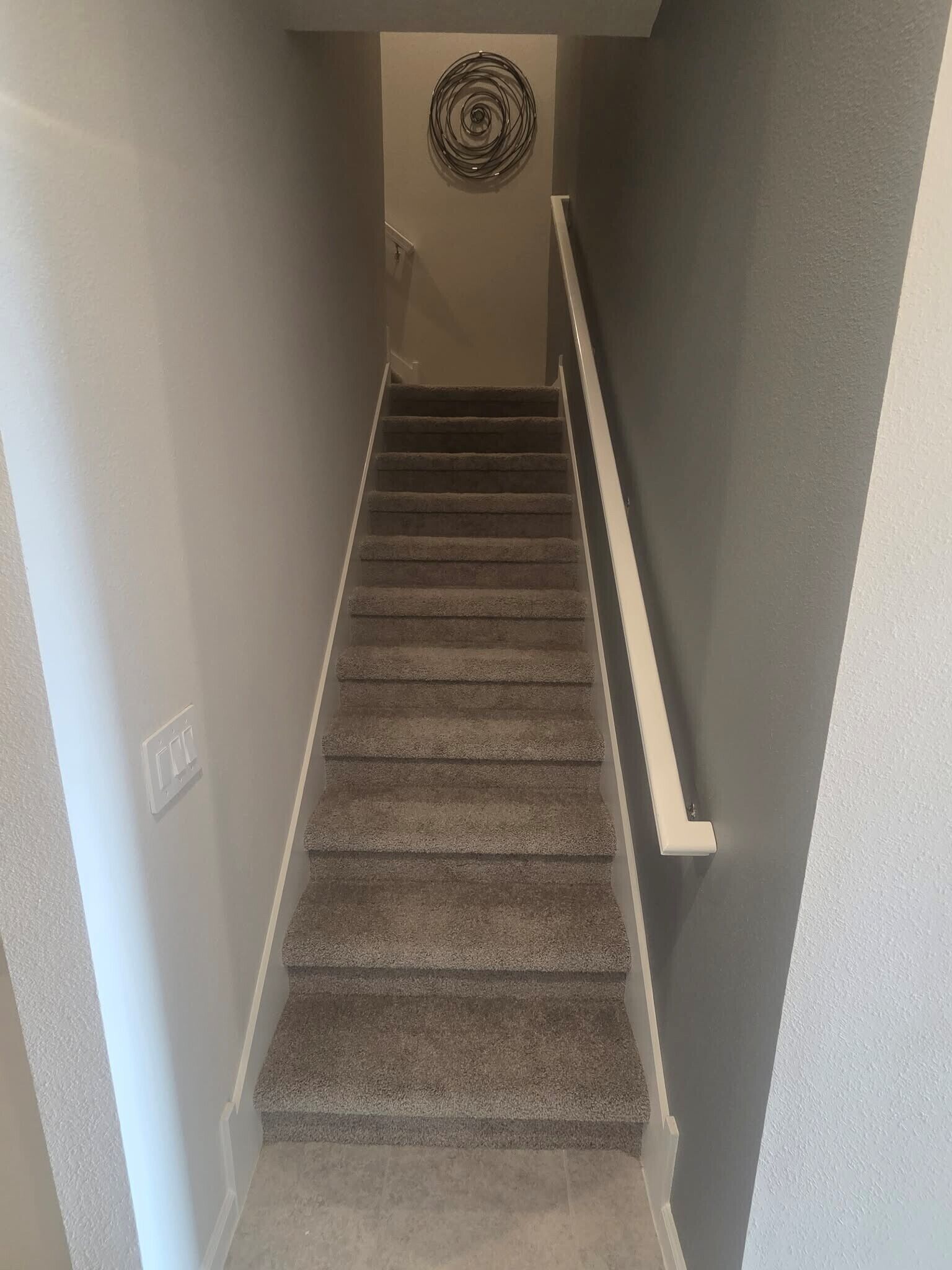 A carpeted staircase with a handrail, leading to a landing with a circular wall decoration.