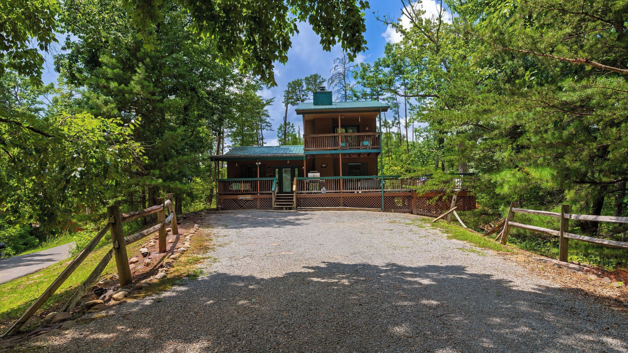 A two-story lodge with a gravel driveway leading to a wooden fence.