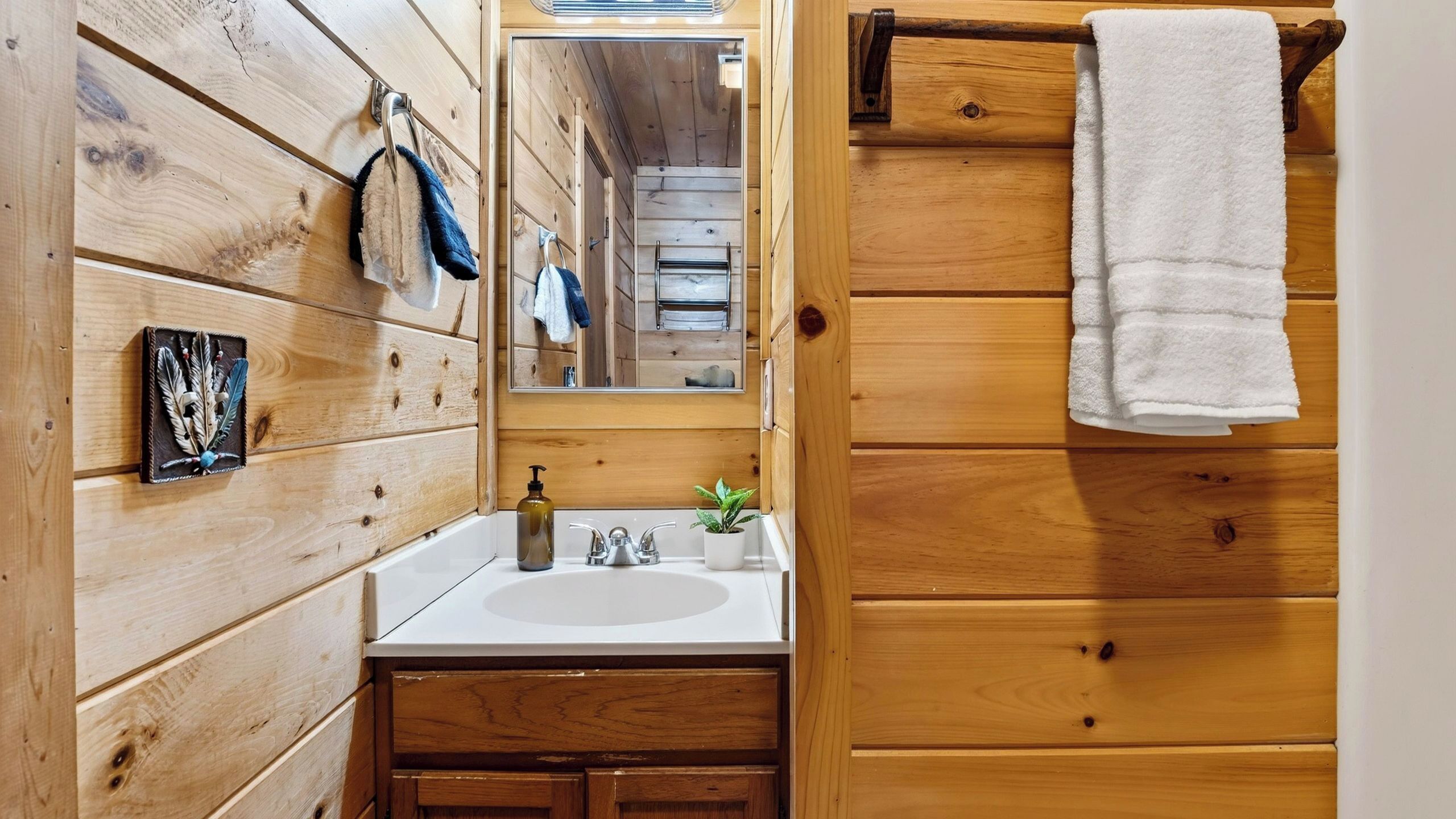 A wooden cabin bathroom with a white sink, a mirror, and a towel rack.