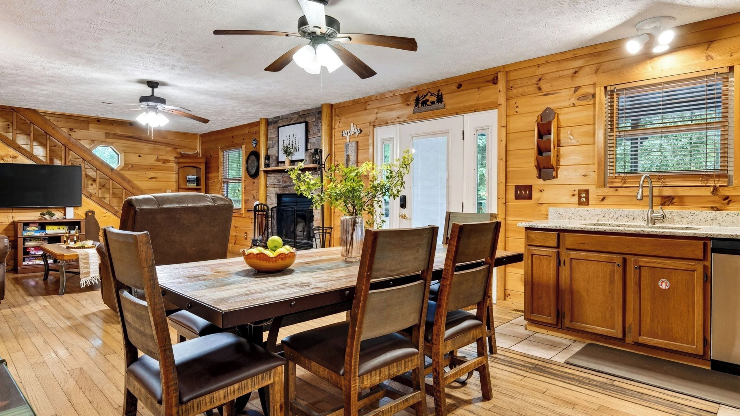 Interior de una cabaña de madera con comedor, cocina y chimenea.