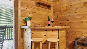 Ein Holzinterieur mit Barbereich, zwei Hockern, einer Weinflasche und einem Blumentopf.