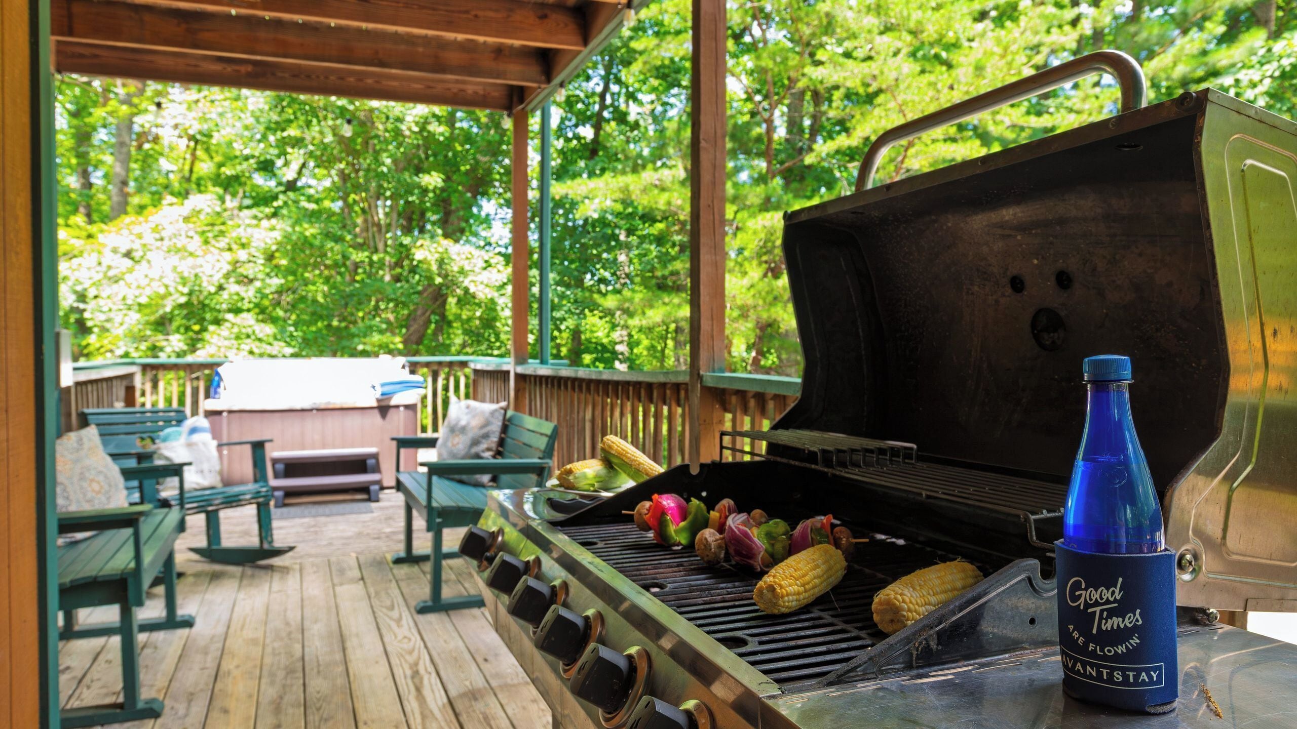 Un barbecue extérieur avec des légumes et des épis de maïs, installé sur une terrasse en bois avec des bancs.