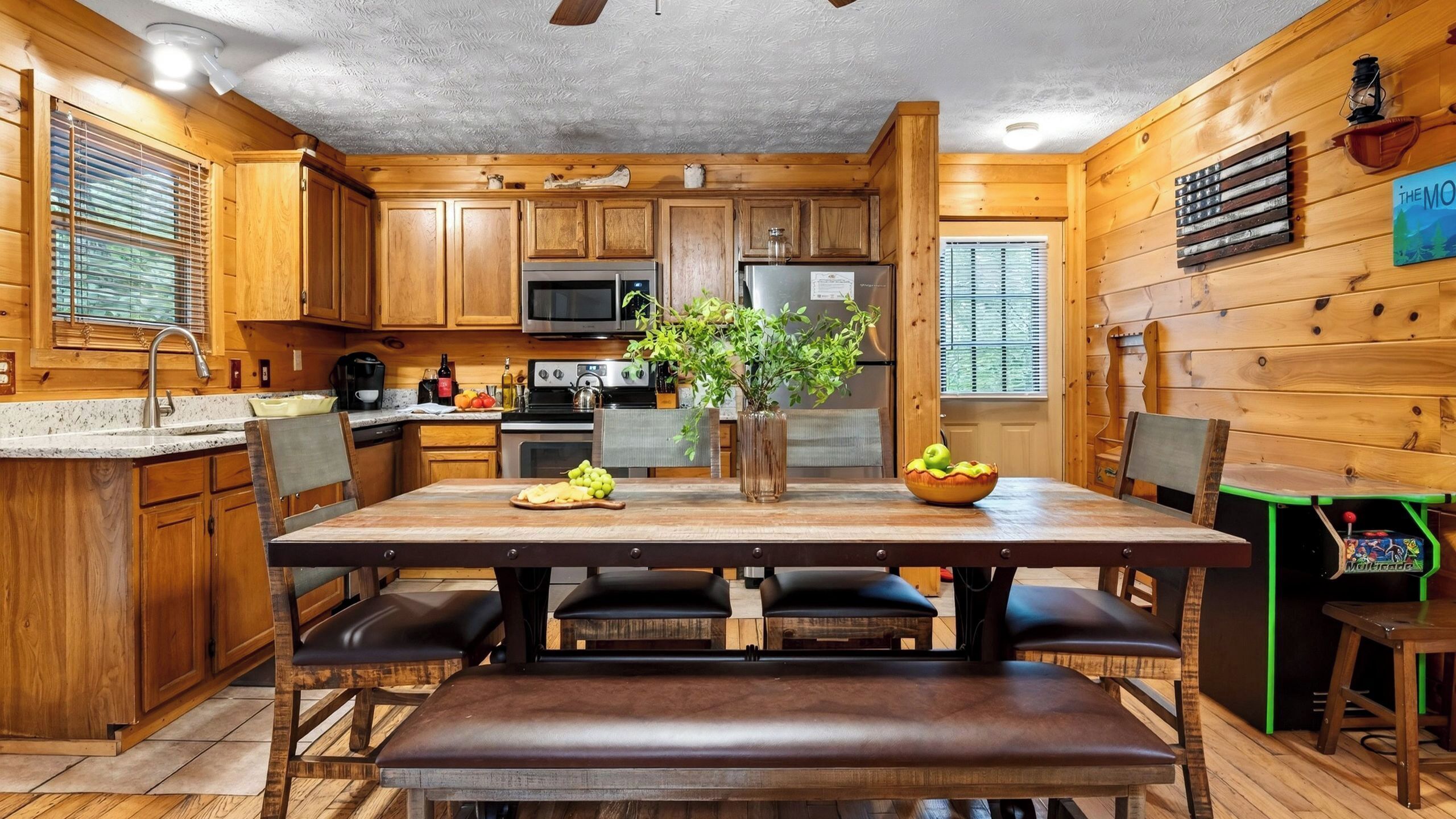 Interior de una cabaña de madera con cocina, comedor y un amplio ventanal.