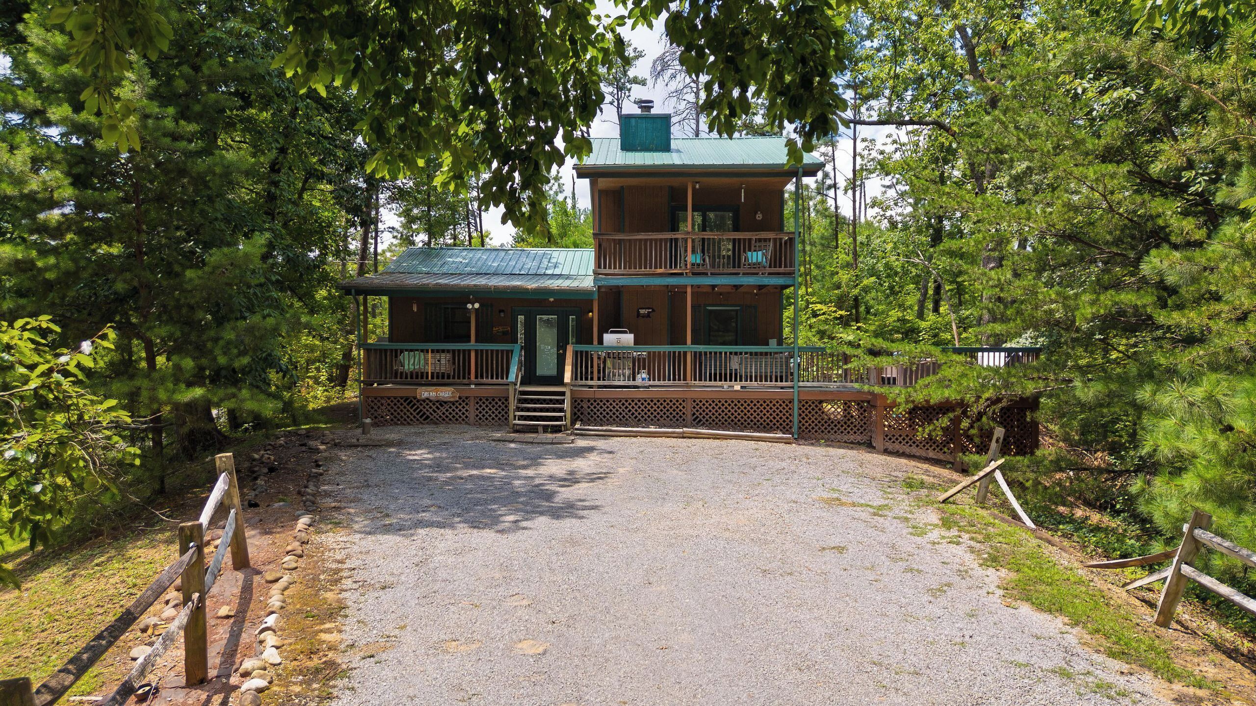 A two-story wooden cabin with a gravel driveway leading to a gated entrance.