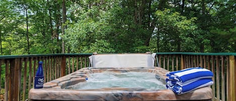 Ein Whirlpool im Freien, umgeben von einer Holzterrasse und dichtem Wald.