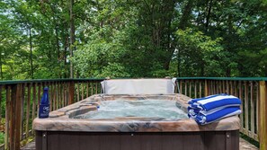 Un bain à remous installé à l’extérieur, entouré d’une terrasse en bois et d’une forêt dense.