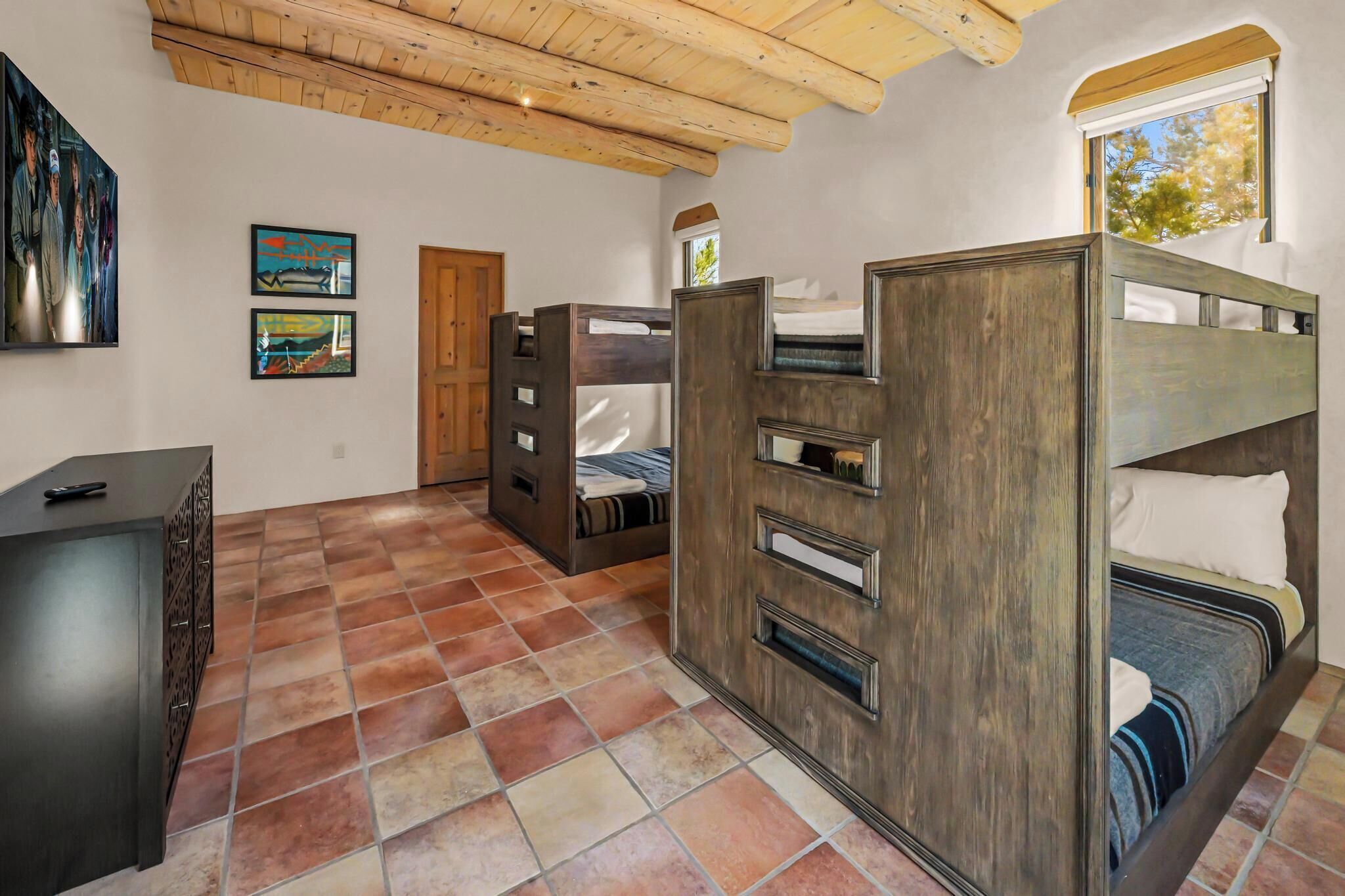 A room with bunk beds, a wooden ceiling, a door, and artwork on the wall.