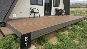 Ein modernes Haus mit einer Holzterrasse, zwei schwarzen Stühlen und einem kleinen Tisch.