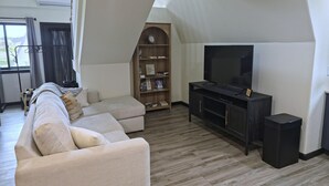 Ein Wohnzimmer mit Sofa, Fernseher, Bücherregal und einem Fenster mit Vorhängen.