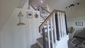 Eine Treppe mit hölzernem Geländer und weißen Spindeln, einer Wandleuchte, einem Willkommensschild und einem gerahmten Bild.