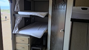 Interior compact d'una autocaravana amb lliteres, un armariet petit i una porta amb mànega de metall.