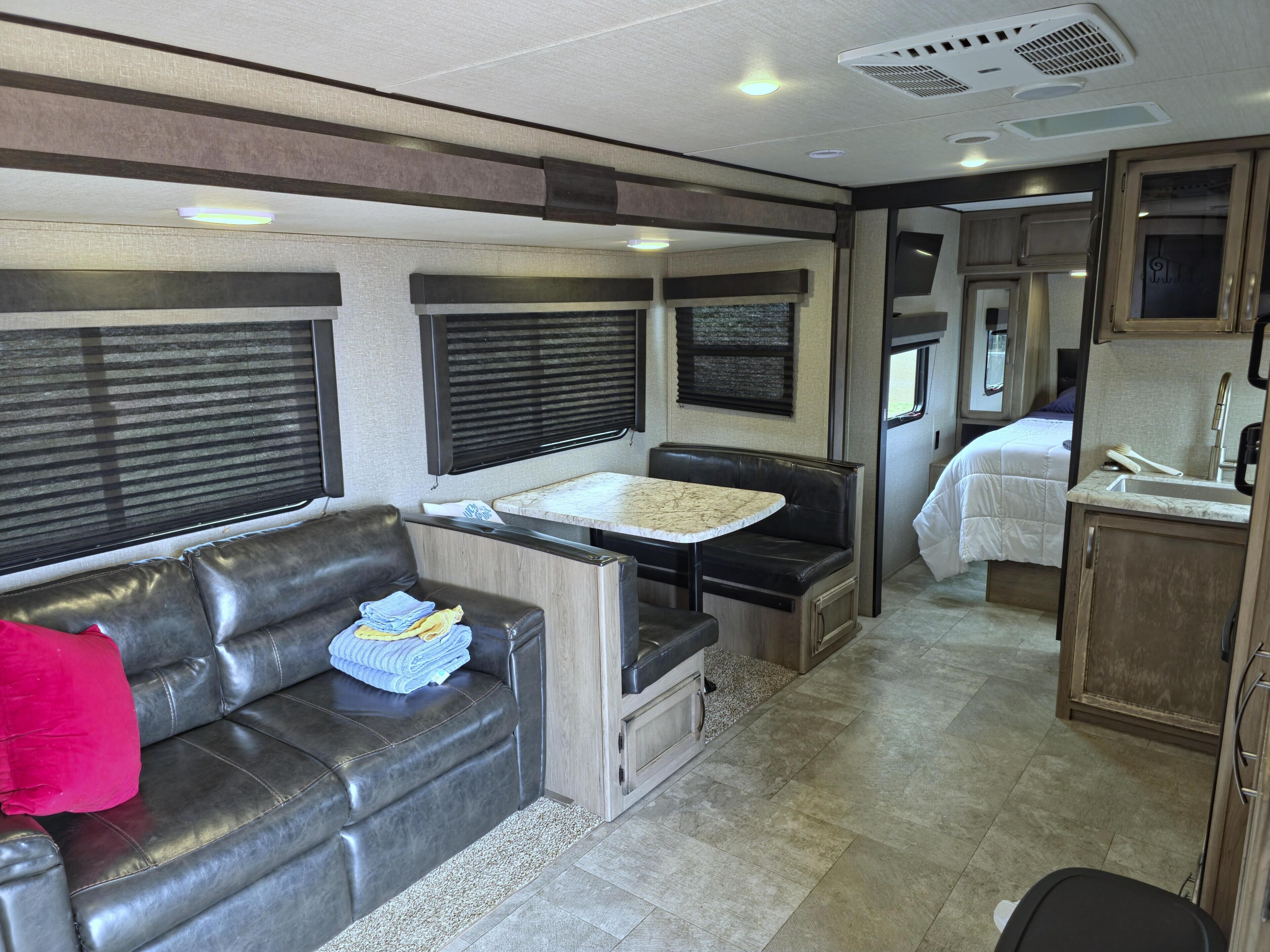 A compact RV interior with a sofa, a small dining table, a kitchenette, and a bed.