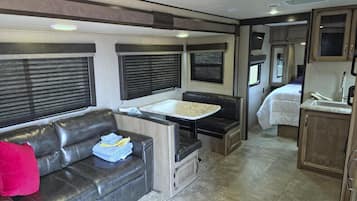 Un intérieur de camping-car compact comprenant un canapé, une petite table à manger, un coin cuisine et un lit.