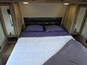 A bed with a headboard, two pillows, and a quilted white bedspread. - Large Planet Camper - Roomy planet-themed camper for groups, sleeps six (Penrose)