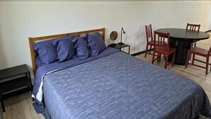 Quarto com cama, mesa de cabeceira, abajur e um espaço de jantar com cadeiras e mesa.