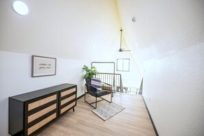 A modern interior with a wooden floor, a black console with woven drawers, a chair with a striped cushion, and a wall-mounted picture frame with text. - Cabin 6 | Rigel - A-frame cabin with loft, full kitchen, sleeps six (Penrose)