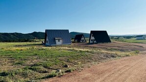 Paisagem rural com dois edifícios distintos, uma estrada de terra e um fundo montanhoso.