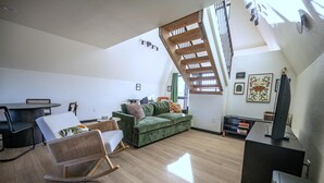 Uma sala de estar moderna com um sofá verde, uma poltrona de balanço e uma escada com guarda-corpo de madeira.