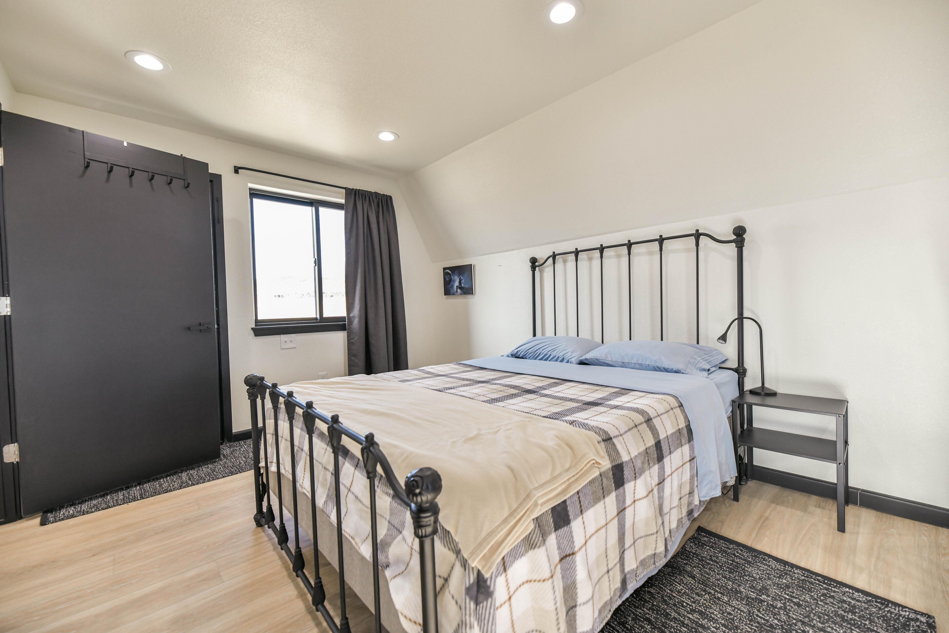 A bedroom with a bed, a bedside table, a window, and a door.