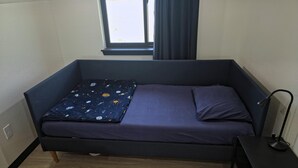 Et lille værelse med en enkelt seng, et lille bord og et vindue med gardiner.