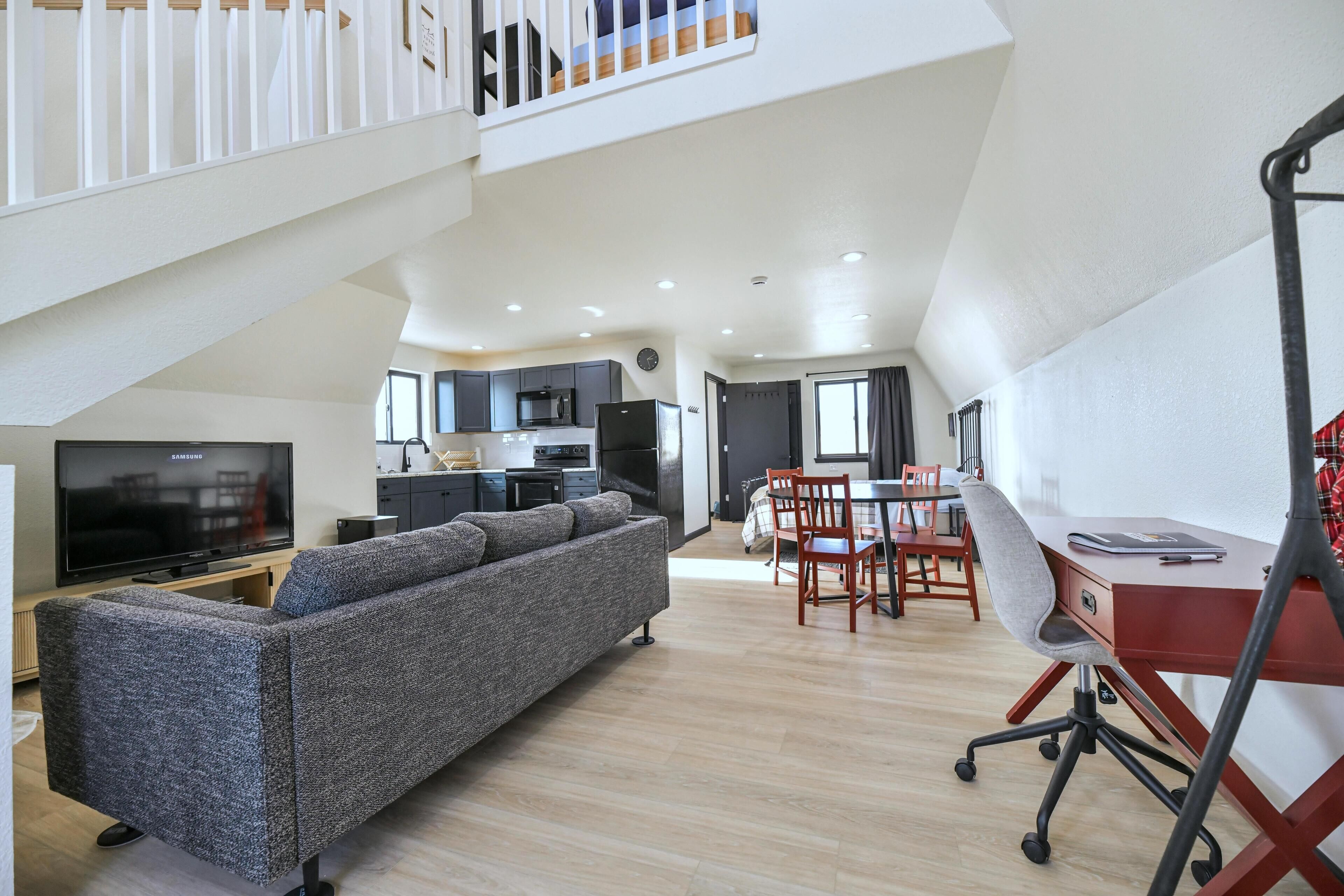 A modern living space with a sofa, dining area, kitchen, and a staircase.