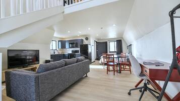 A modern living space with a sofa, dining area, kitchen, and a staircase.