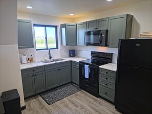 A modern kitchen with grey cabinets, a black stove, a microwave, and a refrigerator.