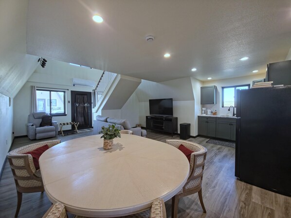 A modern living space with a dining area, kitchen, and a staircase leading to an upper level.