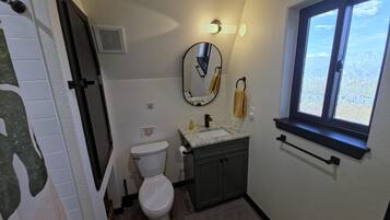 A bathroom with a toilet, sink, mirror, and window.