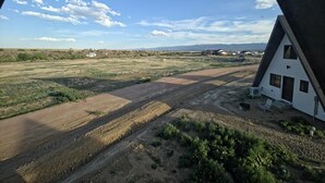Ein Haus mit einem dreieckigen Dach, einer unbefestigten Straße und einer flachen Landschaft mit spärlicher Vegetation.